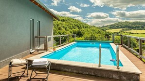 A rectangular swimming pool with a wooden deck and lounge chairs, surrounded by a wooden railing.