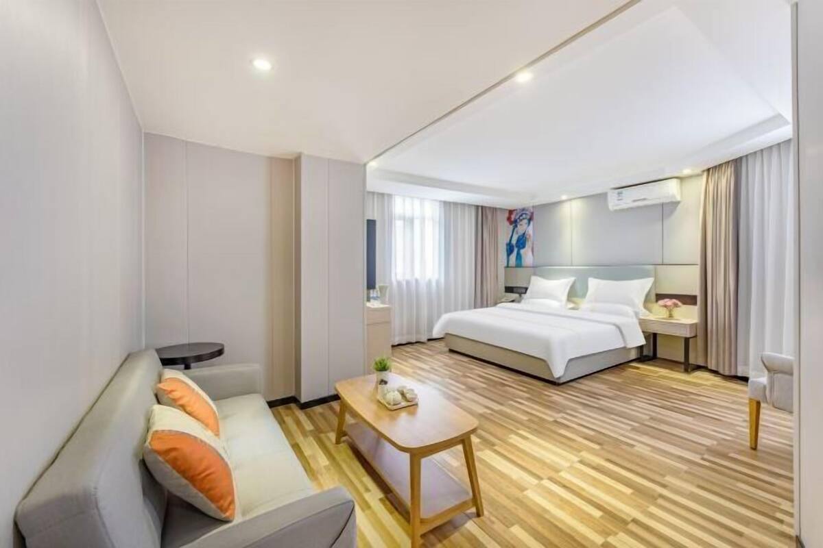 A hotel room with a bed, a sofa, a small table, and a nightstand.