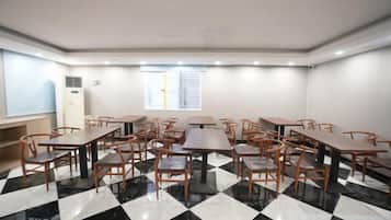 A room with multiple tables and chairs, a window with blinds, and a check-in counter.