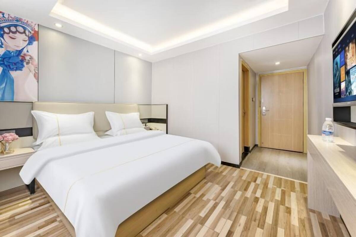A hotel room with a large bed, a bedside table with a vase of flowers, and a wooden floor.