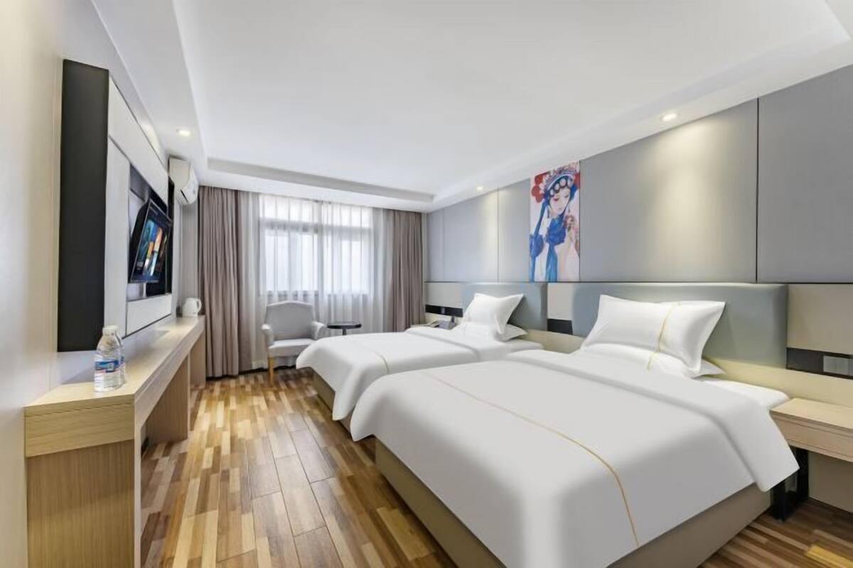 A hotel room with two beds, a desk, a chair, a TV, and a painting on the wall.