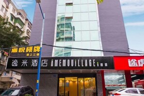 A hotel entrance with a modern facade, a visible sign for 'AMEMOVILLAGE', and a clear view of the street.