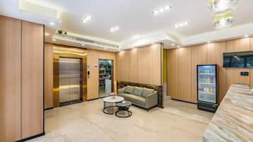 A hotel lobby with a reception desk, a sofa, a coffee table, an elevator, and a refrigerator.