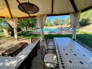 Un patio al aire libre con piscina, bancos de madera, sillas de metal y una mesa de azulejos.