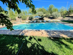 Una piscina rectangular con borde de azulejos, rodeada de césped y árboles.