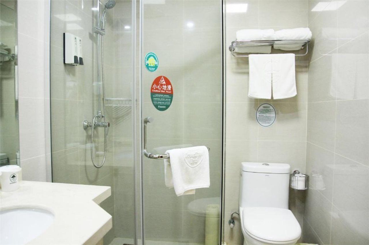 A bathroom with a glass-enclosed shower, a toilet, and a sink. There are towels hanging on a rack and a soap dispenser on the wall.