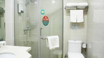 A bathroom with a glass-enclosed shower, a toilet, and a sink. There are towels hanging on a rack and a soap dispenser on the wall.