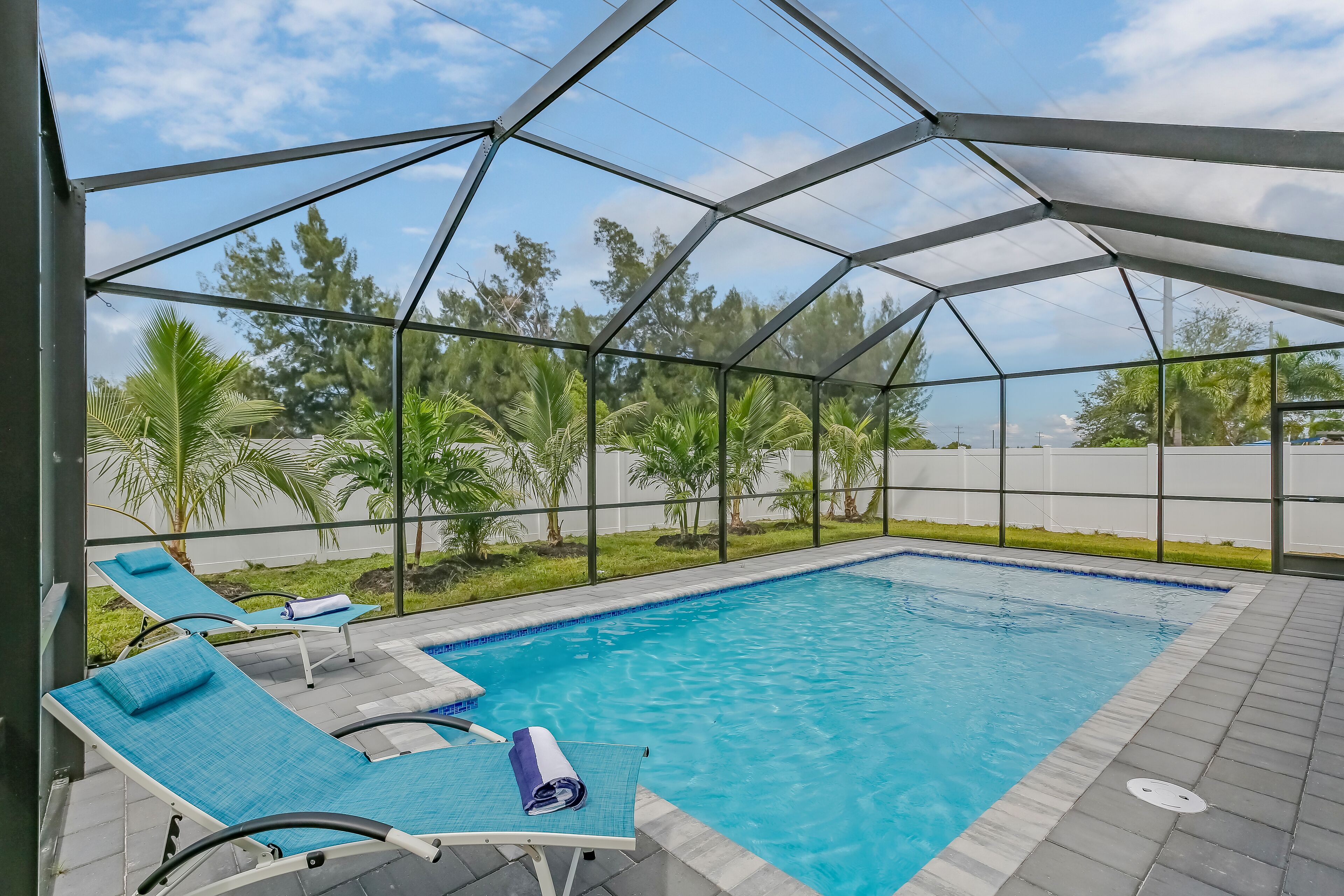Ein überdachter Pool mit Liegestühlen und Blick auf Palmen.