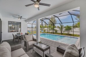 A modern outdoor living area with a pool, wicker furniture, and ceiling fans.