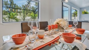 Ein Essbereich mit einem Tisch, gedeckt für vier Personen, mit orangefarbenen Schalen, Weingläsern und einer Vase mit weißen Blumen.