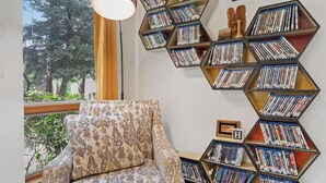 A room with a patterned armchair, a bookshelf with DVDs, and a view of trees through a window. - Perfect Arizona Mountain Retreat (Payson)