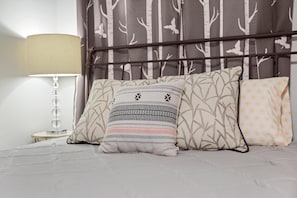 A bed with three pillows, a bedside lamp, and a headboard with a tree pattern.