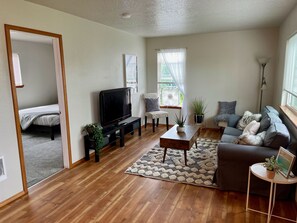 A living room with a TV, sofa, and a bed in the adjacent room.