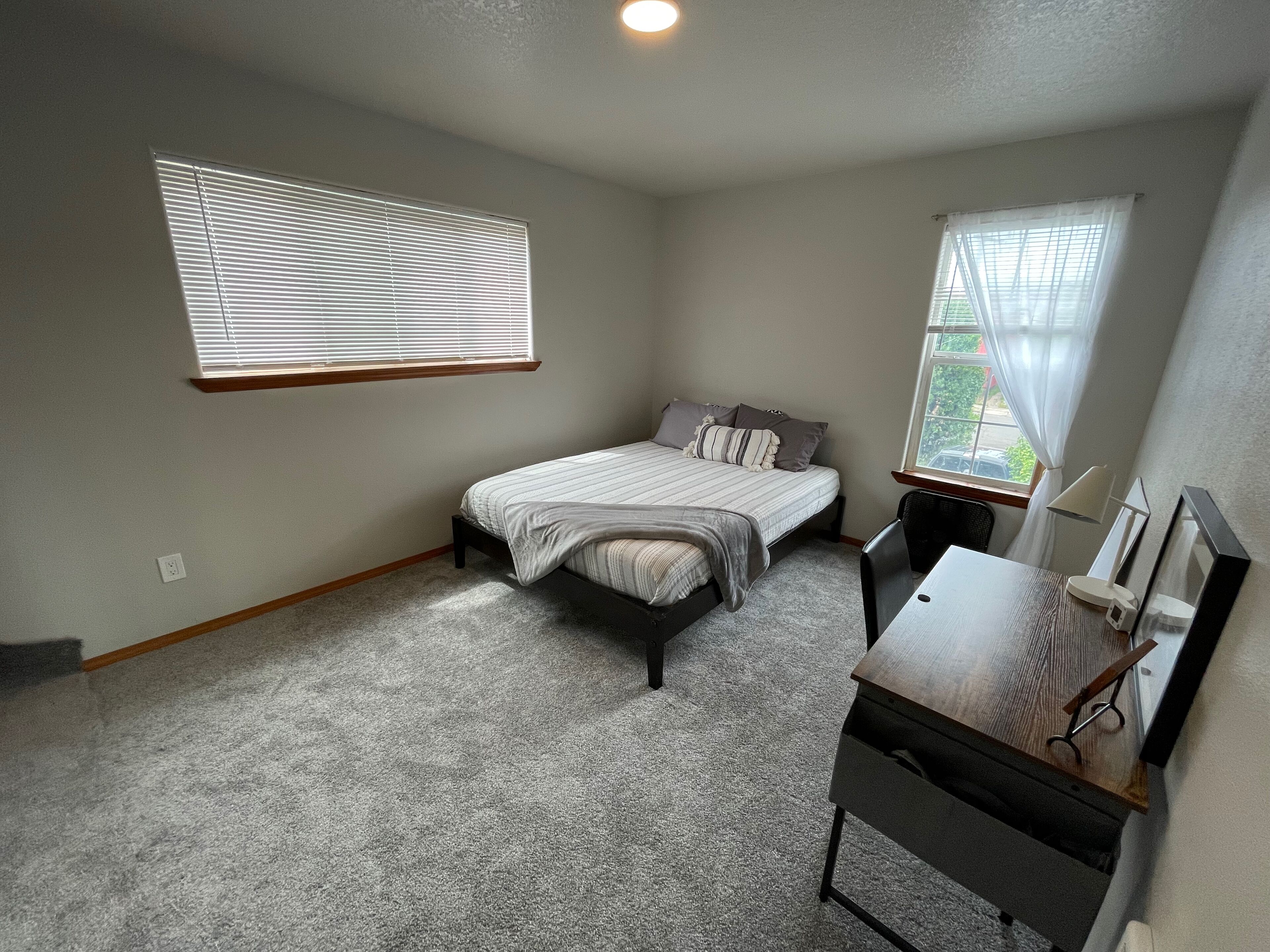 A bedroom with a bed, a desk, and two windows.