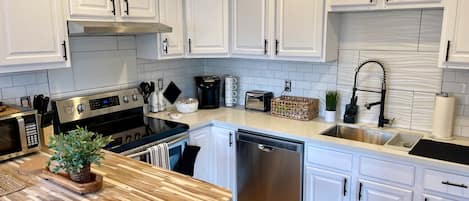 A modern kitchen with white cabinetry, stainless steel appliances, and a wooden countertop.