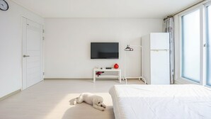 A hotel room with a bed, a TV, a white wardrobe, a white console table, and a large window. - Sokcho World Pet-friendly Pension (Sokcho)