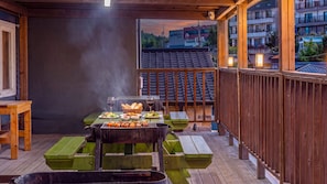 An outdoor dining area with a grill, wooden tables, and a view of buildings in the background. - Sokcho World Pet-friendly Pension (Sokcho)