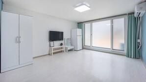 A spacious room with a large sliding glass door, a flat-screen TV, a white wardrobe, and a small desk with a chair. - Sokcho World Pet-friendly Pension (Sokcho)