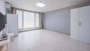 A spacious room with a large sliding glass door, a wardrobe, and a flat-screen TV on a white cabinet. - Sokcho World Pet-friendly Pension (Sokcho)
