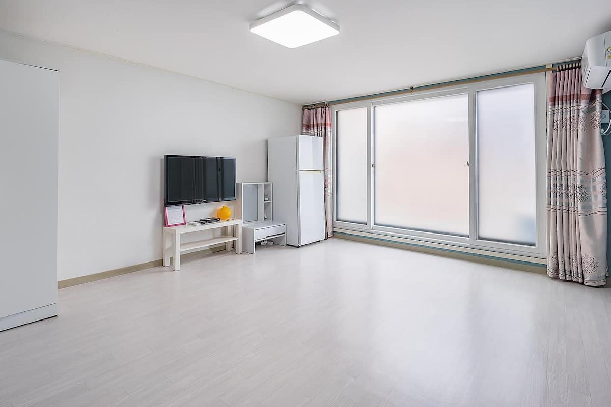 A room with a wardrobe, a television, a small table with a lamp, and a sliding door with curtains.