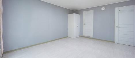 A room with light grey walls, white doors, and a light wooden floor.