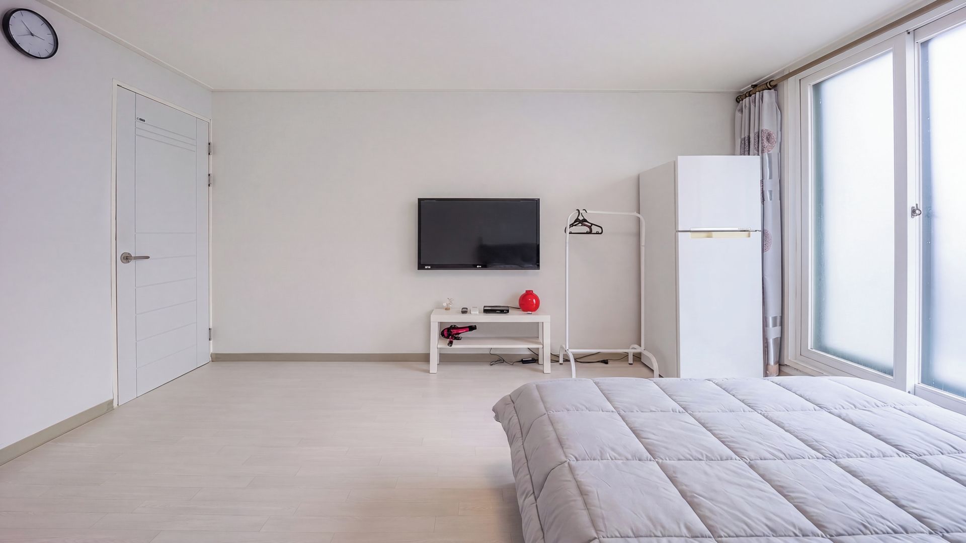 A minimalist bedroom with a bed, a TV, a wardrobe, and a window.