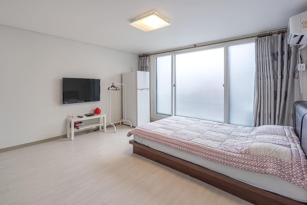A modern bedroom with a bed, a TV, a small table, and a window with curtains.