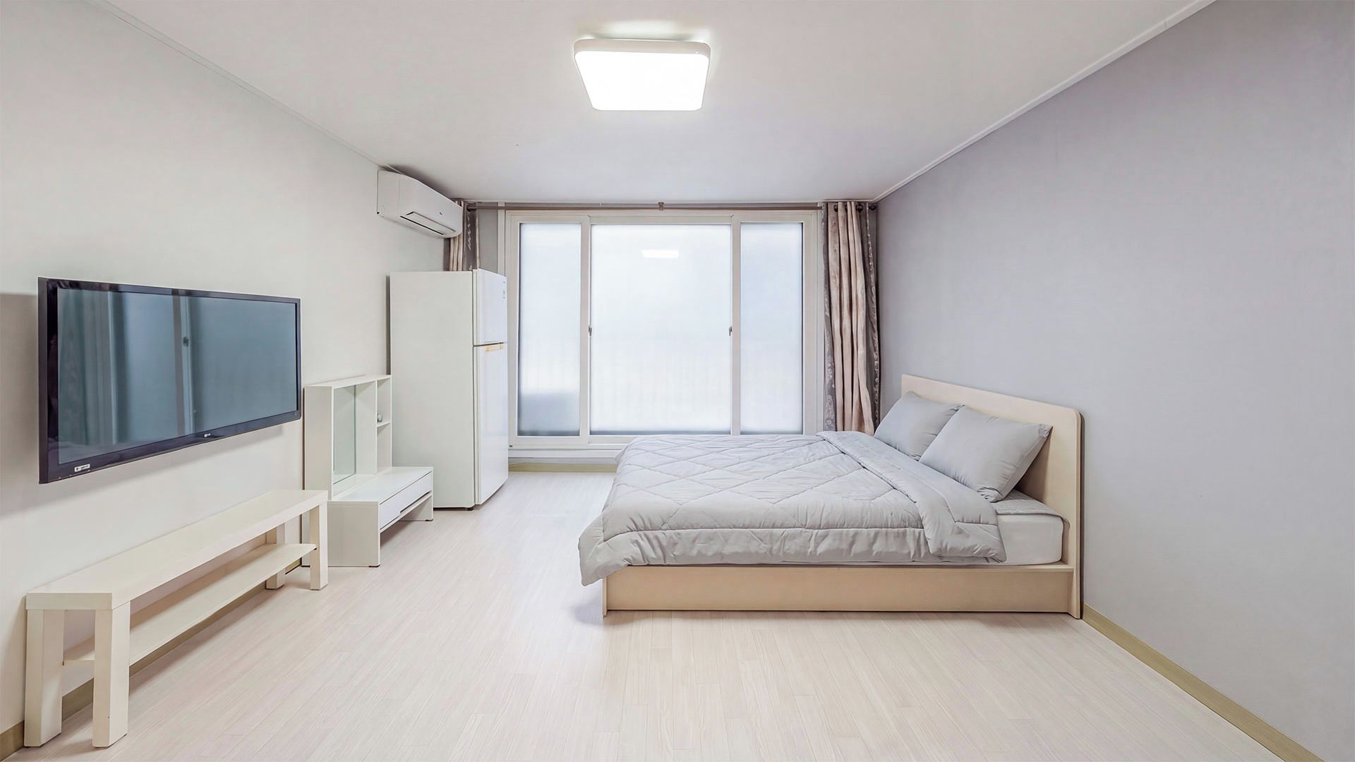 A modern bedroom with a bed, a TV, a wardrobe, and a window with curtains.