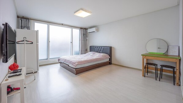 A bedroom with a bed, a desk with two chairs, a wardrobe, and a TV.