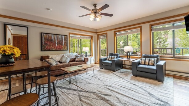 A spacious living room with a wooden dining table, two sofas, a coffee table, and a large window with a view of trees. - Slopeside #2775 by Summit County Mountain Retreats (Keystone)