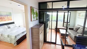 Une chambre à coucher comprenant un lit, une commode et un balcon avec un canapé et une table.