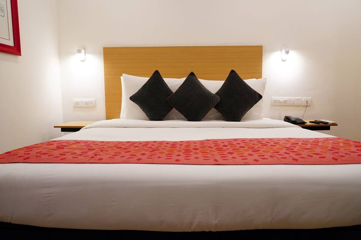 A bed with a wooden headboard, white bedding, and three black pillows. There are two bedside tables with a phone and a remote control.