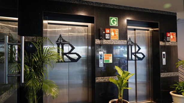 Un ascensore moderno con un logo, pulsanti di chiamata di emergenza e un cartello verde sopra.