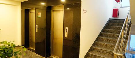 A hotel lobby with a staircase, elevators, and a potted plant.
