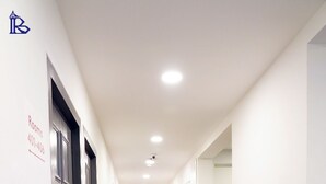 Un lungo e stretto corridoio con pavimento in legno e pareti bianche, che conduce a una stanza con una porta su cui è indicato 'Rooms 401-406'.