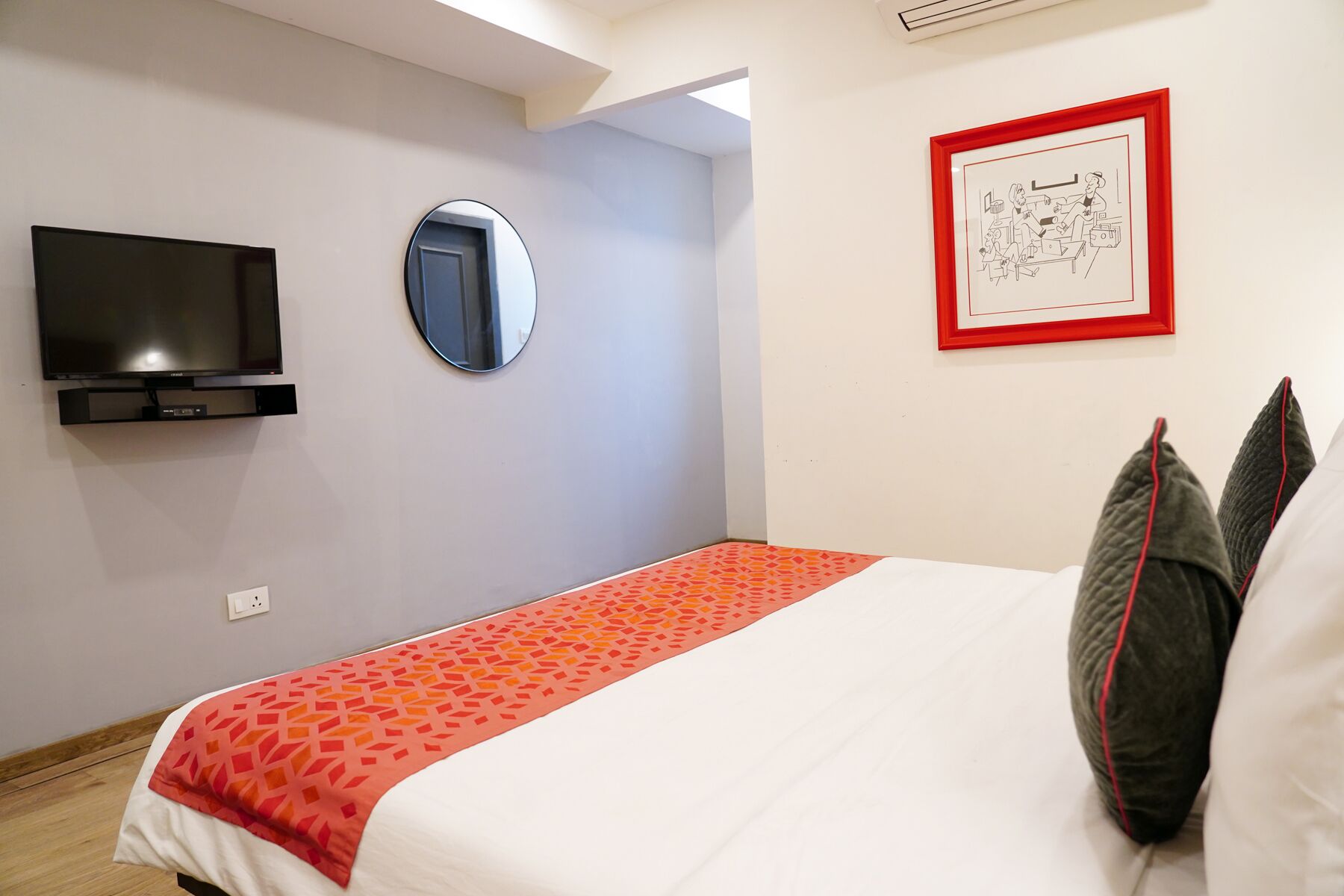 Una habitación de hotel con una cama, televisión, espejo y una obra de arte enmarcada en la pared.