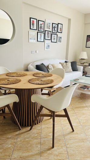 Un espace repas avec une table ronde, des chaises blanches et un mur orné de tableaux encadrés.