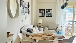 Una sala de estar moderna con comedor, que incluye un sofá, sillas, una mesa con individuales, una lámpara y obras de arte en las paredes.