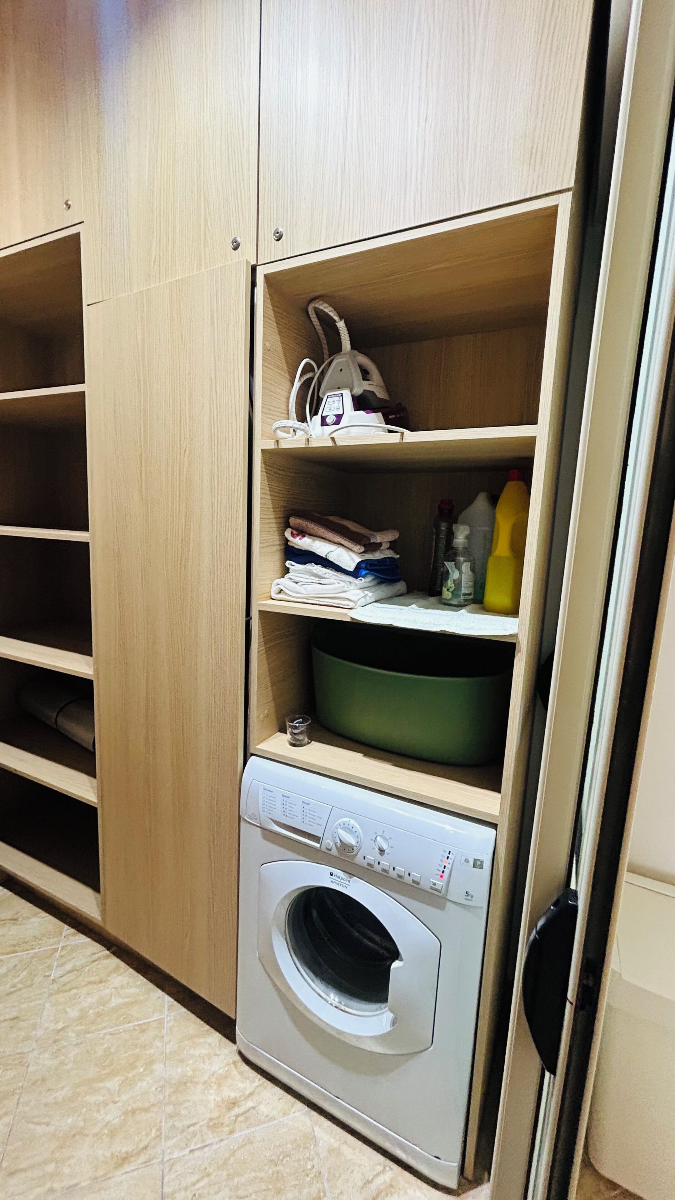 A laundry area with a washing machine, shelves with folded clothes, and a bottle of detergent.
