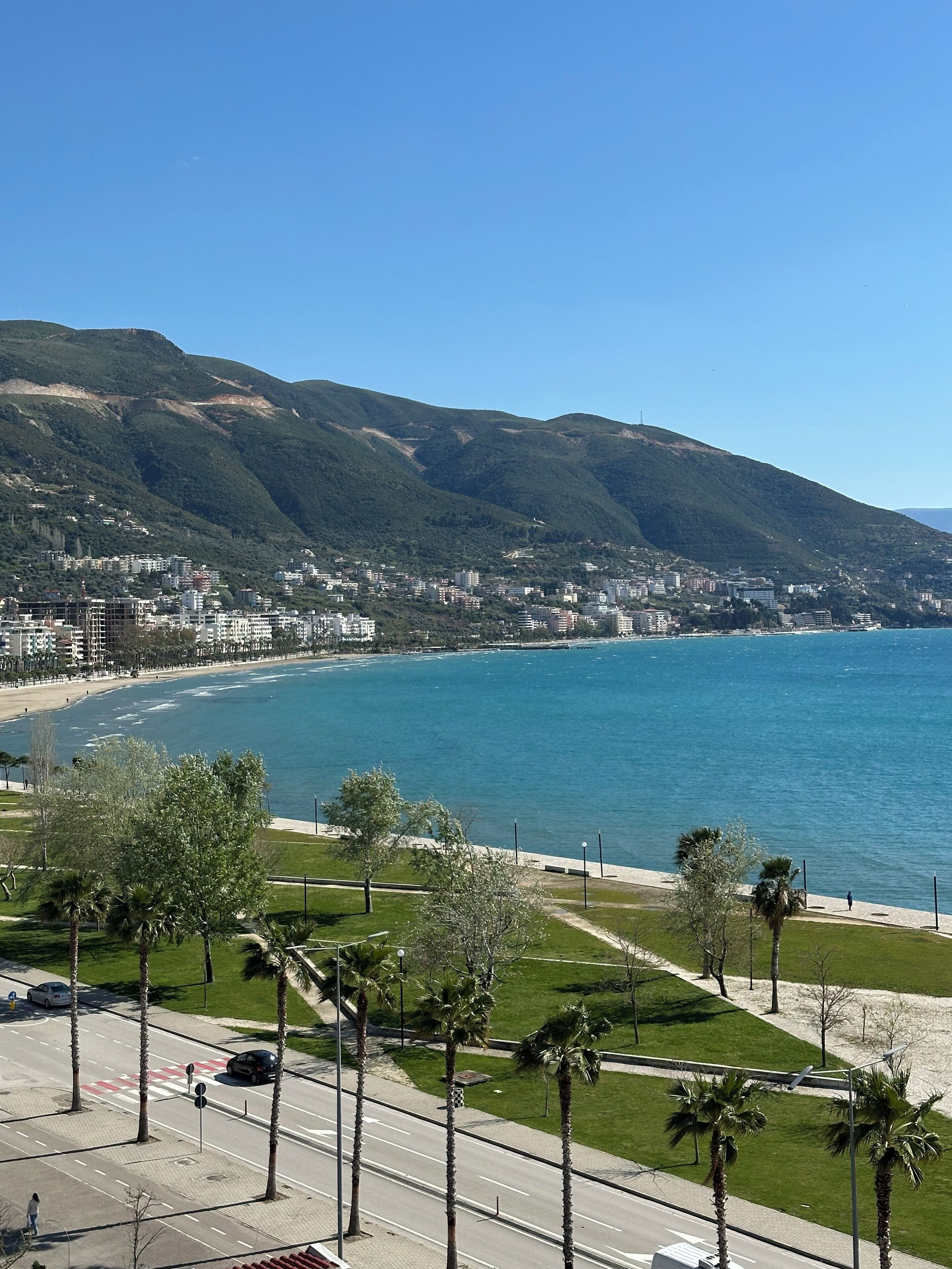 A coastal cityscape with a beach, palm trees, and a mountainous backdrop.