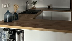 Una cocina moderna con armarios blancos, encimera de madera, un fregadero y dos lámparas colgantes de mimbre.