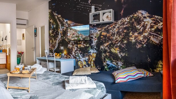 Ett hotellrum med en säng, ett skrivbord och en sittgrupp. Det finns en väggmålning på väggen och ett fönster med utsikt över stadsbilden.