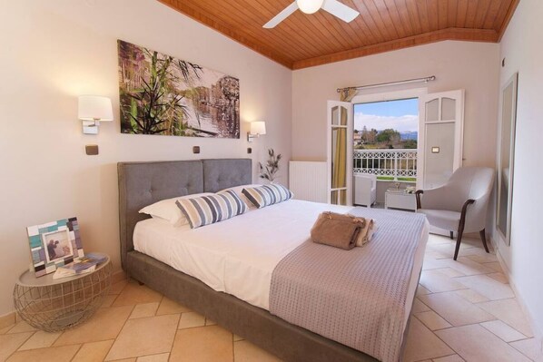 A bedroom with a large bed, a ceiling fan, a painting, and a view of the outside. - Bright suite (Ληξούρι)
