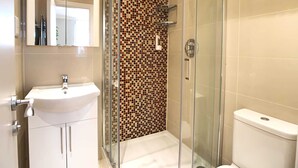 Ein modernes Badezimmer mit einer gläsernen Duschkabine, einem weißen Waschbecken und einer gefliesten Wand.