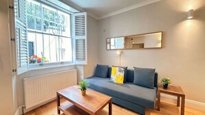 Ein Zimmer mit einer Couch, einem kleinen Tisch, einem Spiegel und einem Fenster mit Fensterläden.