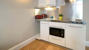 Une cuisine compacte avec des meubles blancs, un four encastré, une plaque de cuisson et une hotte en acier inoxydable.