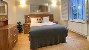 Une chambre à coucher avec un lit en bois, des tables de chevet, un miroir et une fenêtre avec des stores.