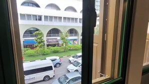 Vista a través de una ventana que muestra un edificio de varios pisos, un estacionamiento con coches y un autobús, y una zona verde con árboles.