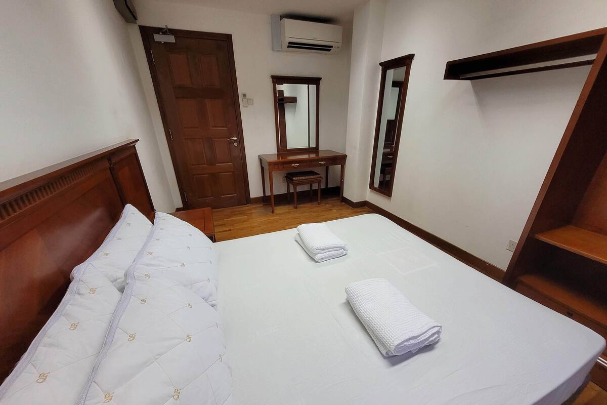 Quarto de hotel com duas camas, uma escrivaninha de madeira, uma cadeira, um espelho e um guarda-roupa.