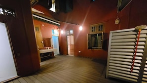 Una terraza de madera con un banco, una puerta blanca y una pared roja con ventanas.